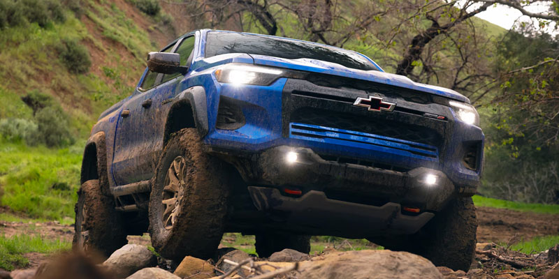 Blue Chevrolet pickup navigating muddy off-road terrain over rocks