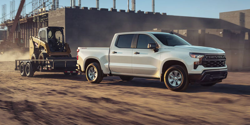 White Chevrolet Silverado towing construction equipment on job site
