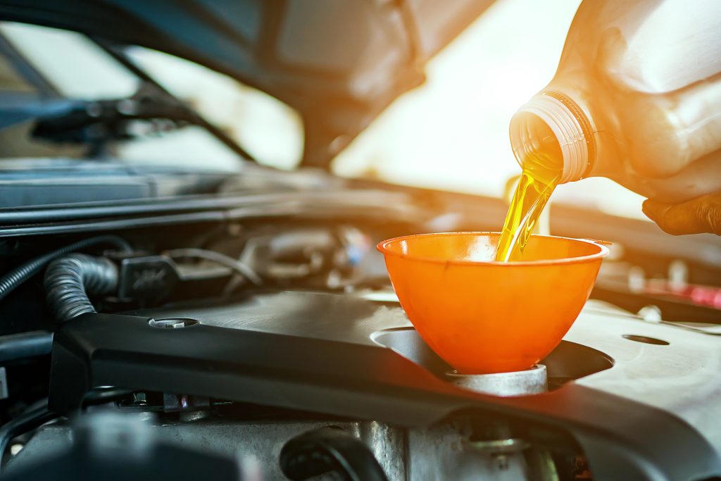 Engine oil being poured into car engine through orange funnel